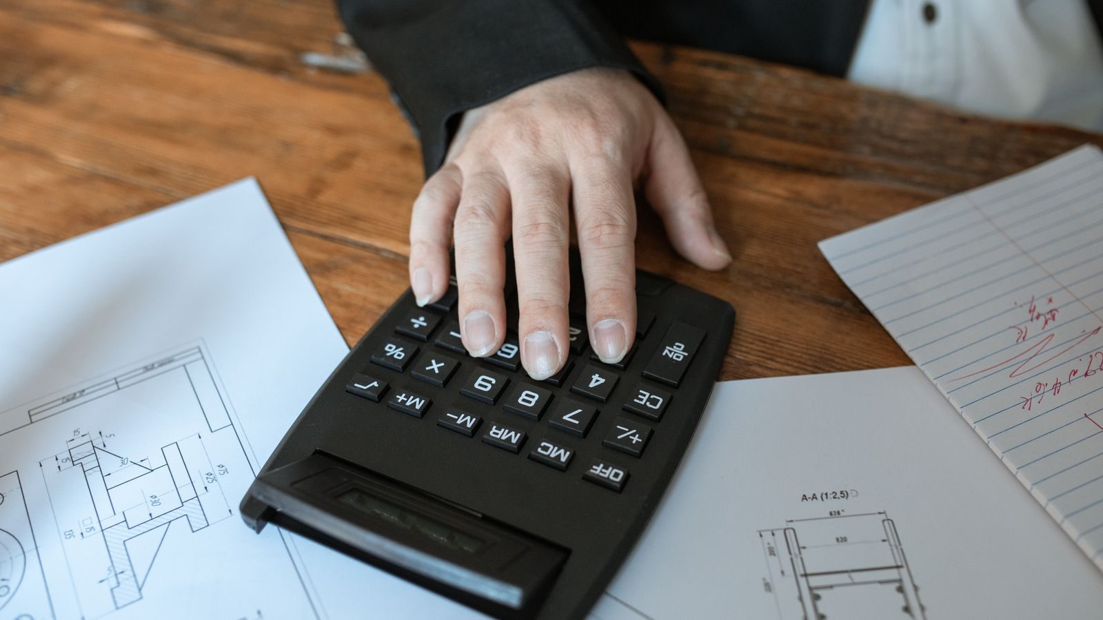 A hand working a calculator on a desk covered in paperwork