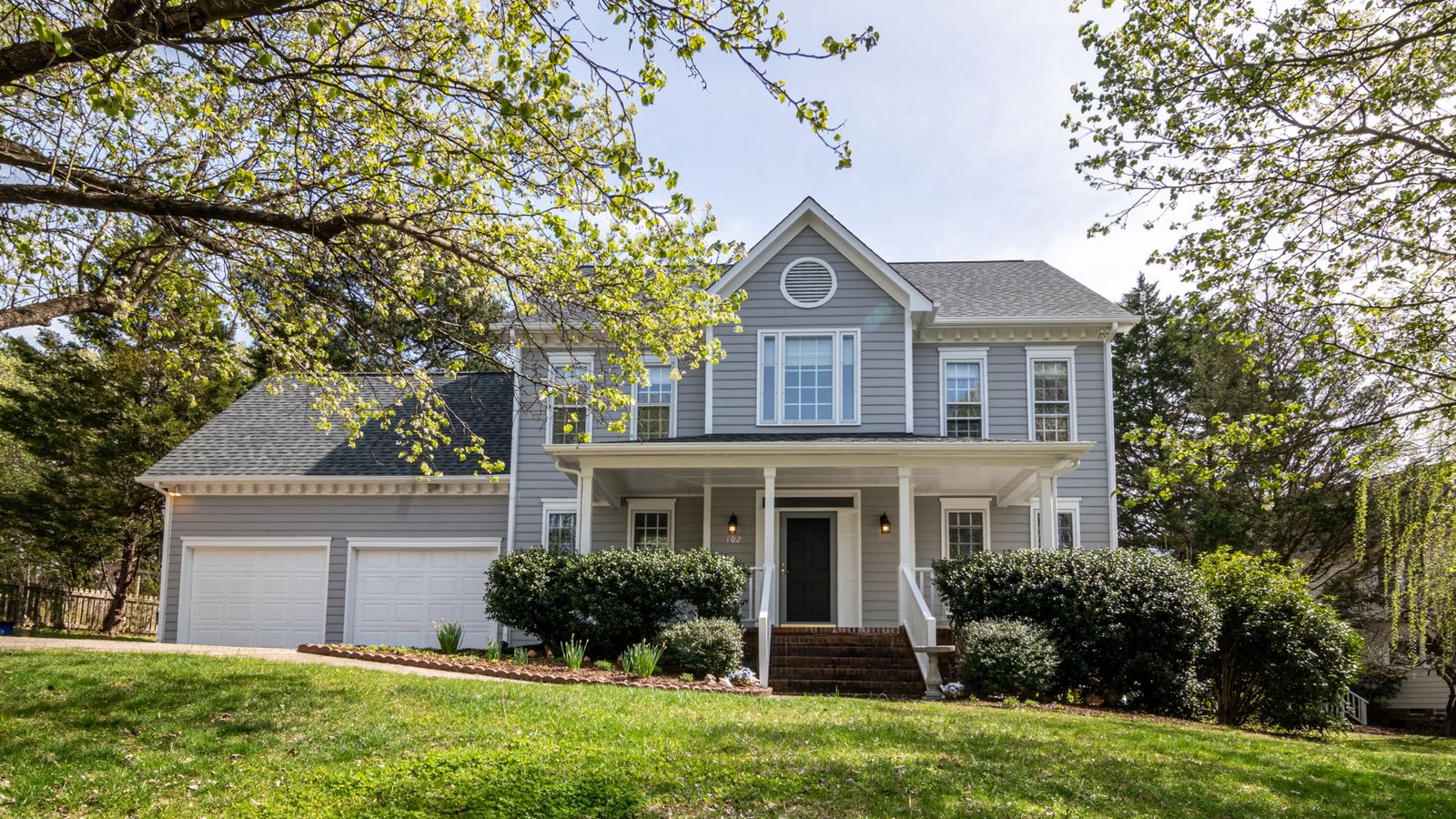 A colonial-style American home with a columned porch framed by mature trees
