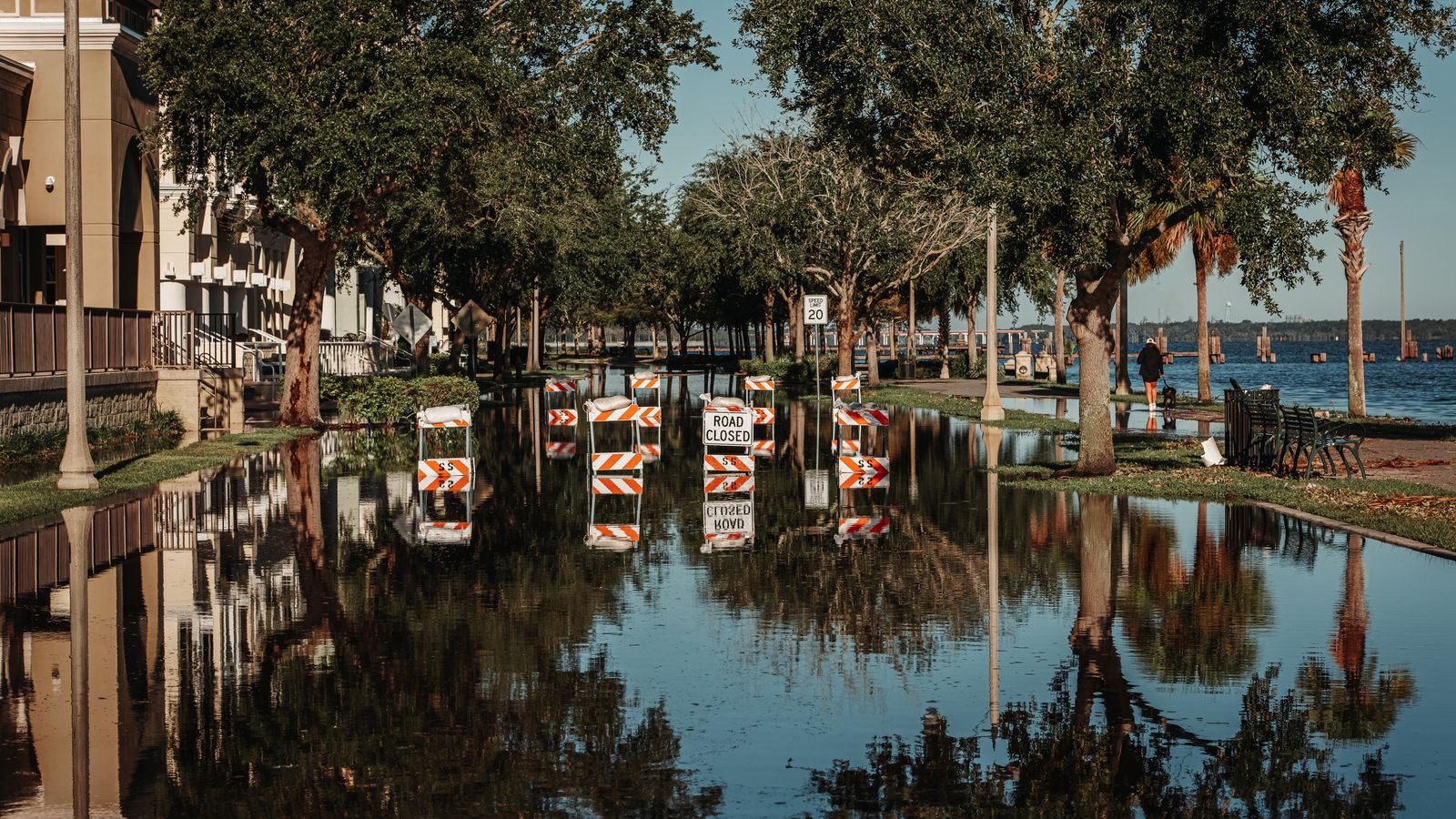 A Louisiana residential street under floodwater with road-closed barricades reflected in the standing water